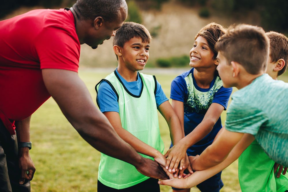 Young Latino boys huddled together smiling at their Black male coach Young Latino boys huddled together smiling at their Black male coach