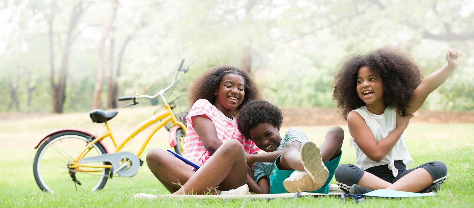 Group of Black kids laughing together with a yellow bicycle at a park